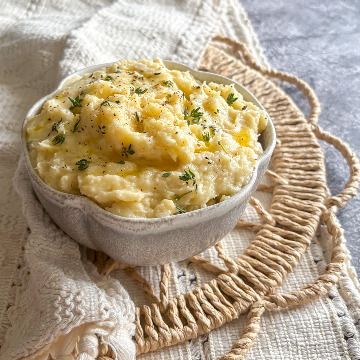 Silky parsnip and pear mash with black pepper and fresh thyme in a small grey ceramic dish.