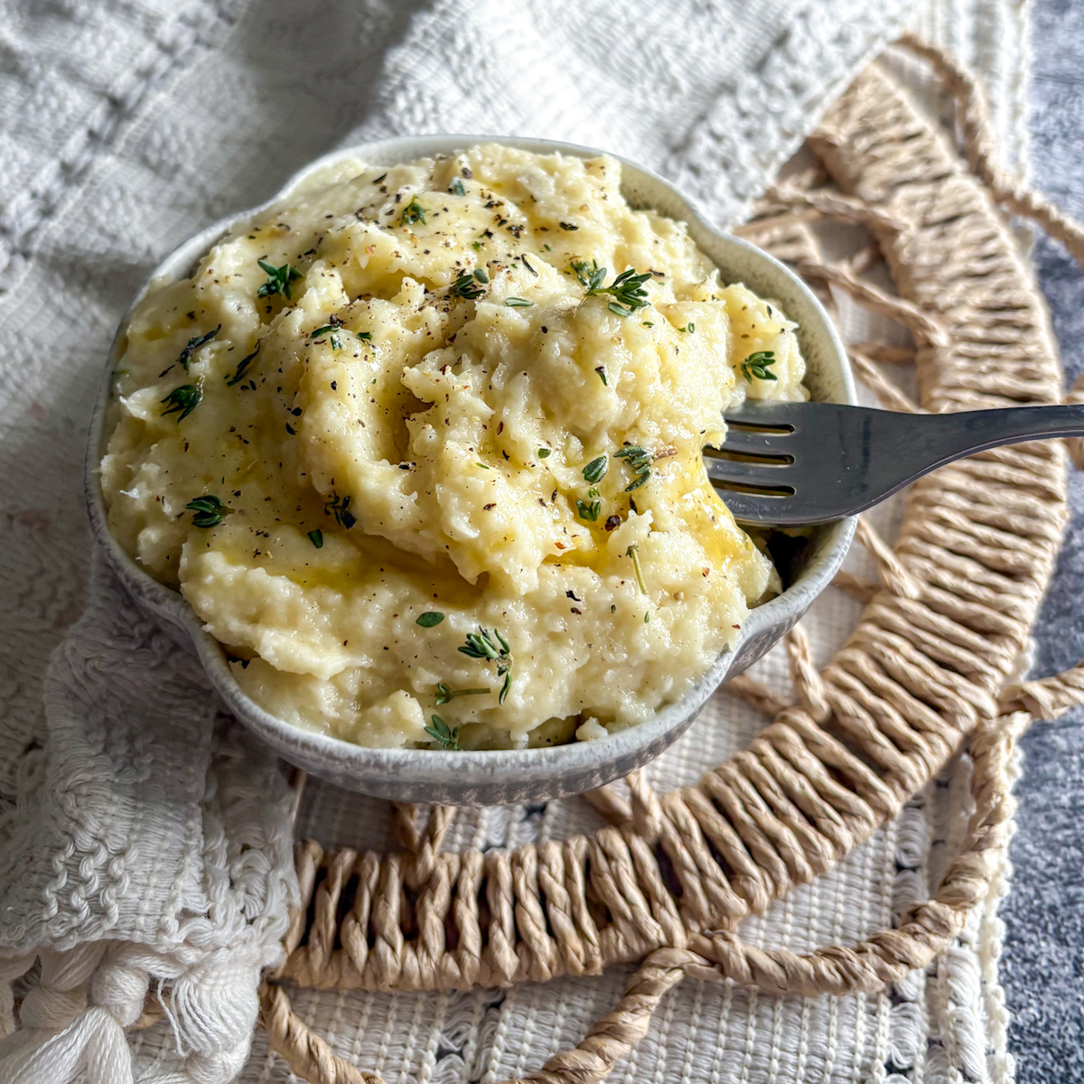 Parsnip and pear mash being scooped with a silver fork from a rustic ceramic serving bowl.