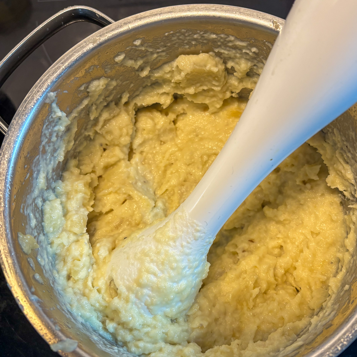 Blending parsnip and pear mash with an immersion blender in a stainless steel pot on the hob.