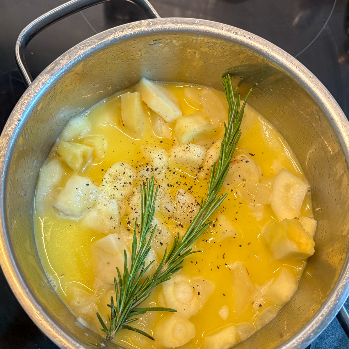 Parsnips simmering with butter and a fresh rosemary sprig in a pot for parsnip and pear mash.