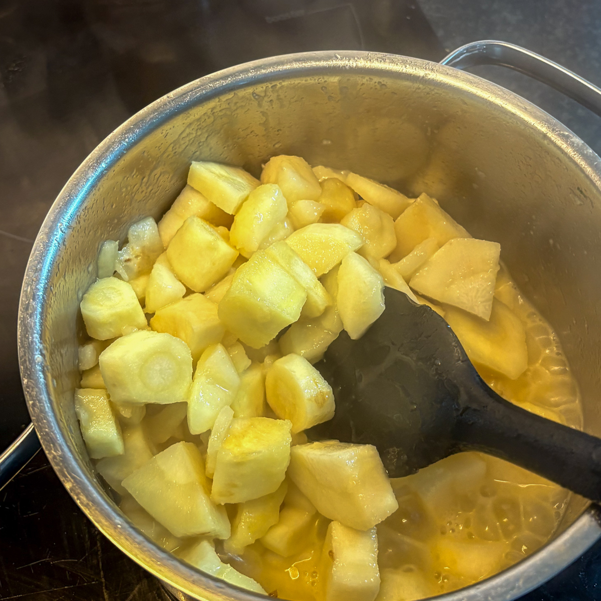 Chopped parsnips cooking in butter in a stainless steel pot, the start of parsnip and pear mash.