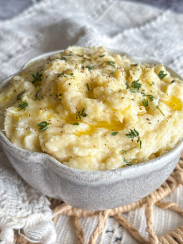 Creamy parsnip and pear mash topped with fresh thyme leaves and ground black pepper in a white ceramic bowl.
