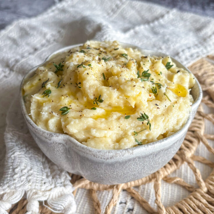 Creamy parsnip and pear mash topped with fresh thyme leaves and ground black pepper in a white ceramic bowl.
