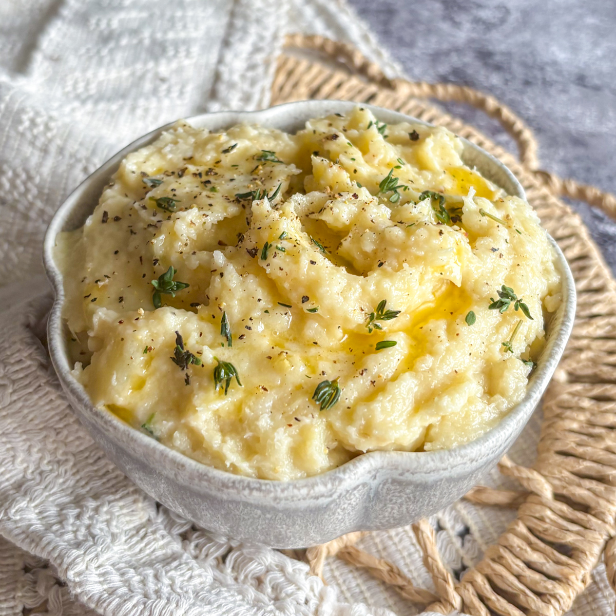 Smooth parsnip and pear mash with thyme leaves and pepper served on a woven natural placemat.