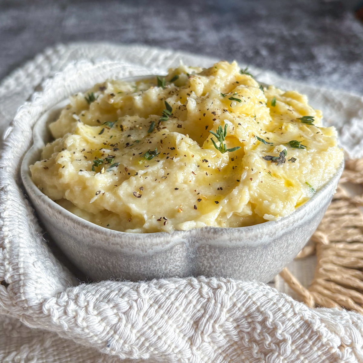 Close-up of silky parsnip and pear mash garnished with fresh thyme in a rustic white serving bowl.