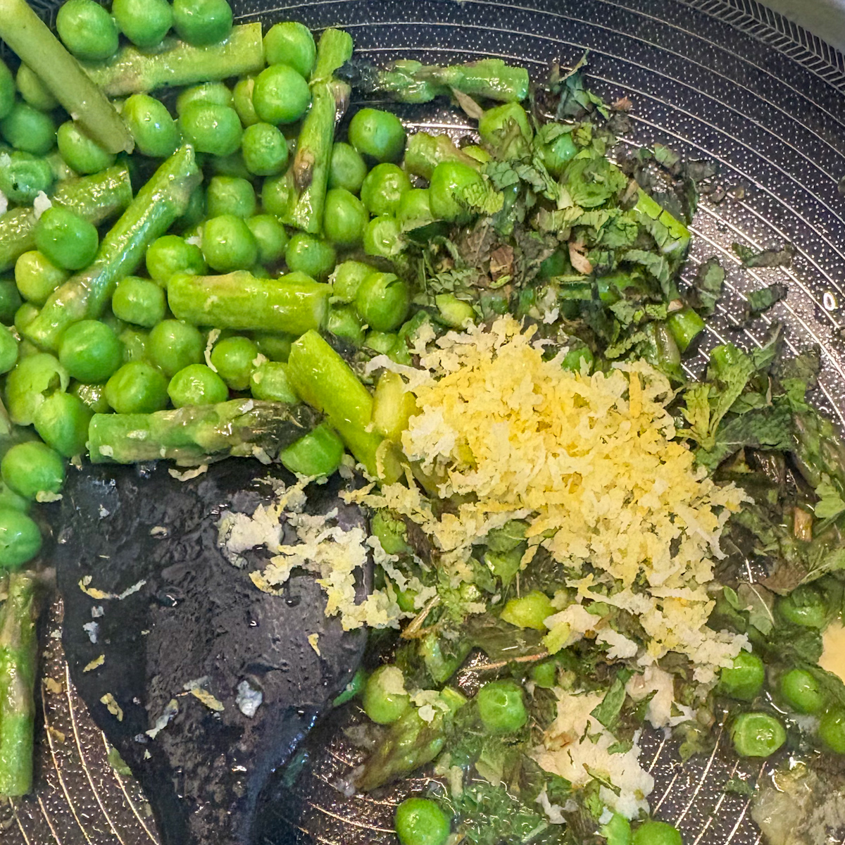 Peas and asparagus with mint, lemon zest and garlic cooking in a pan for crostini