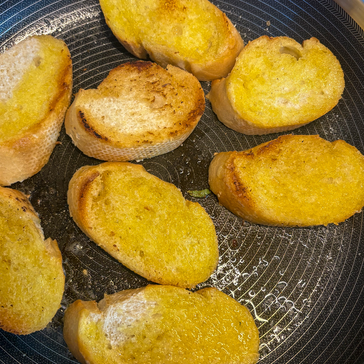 Buttered baguette slices frying golden in a pan for pea and asparagus crostini