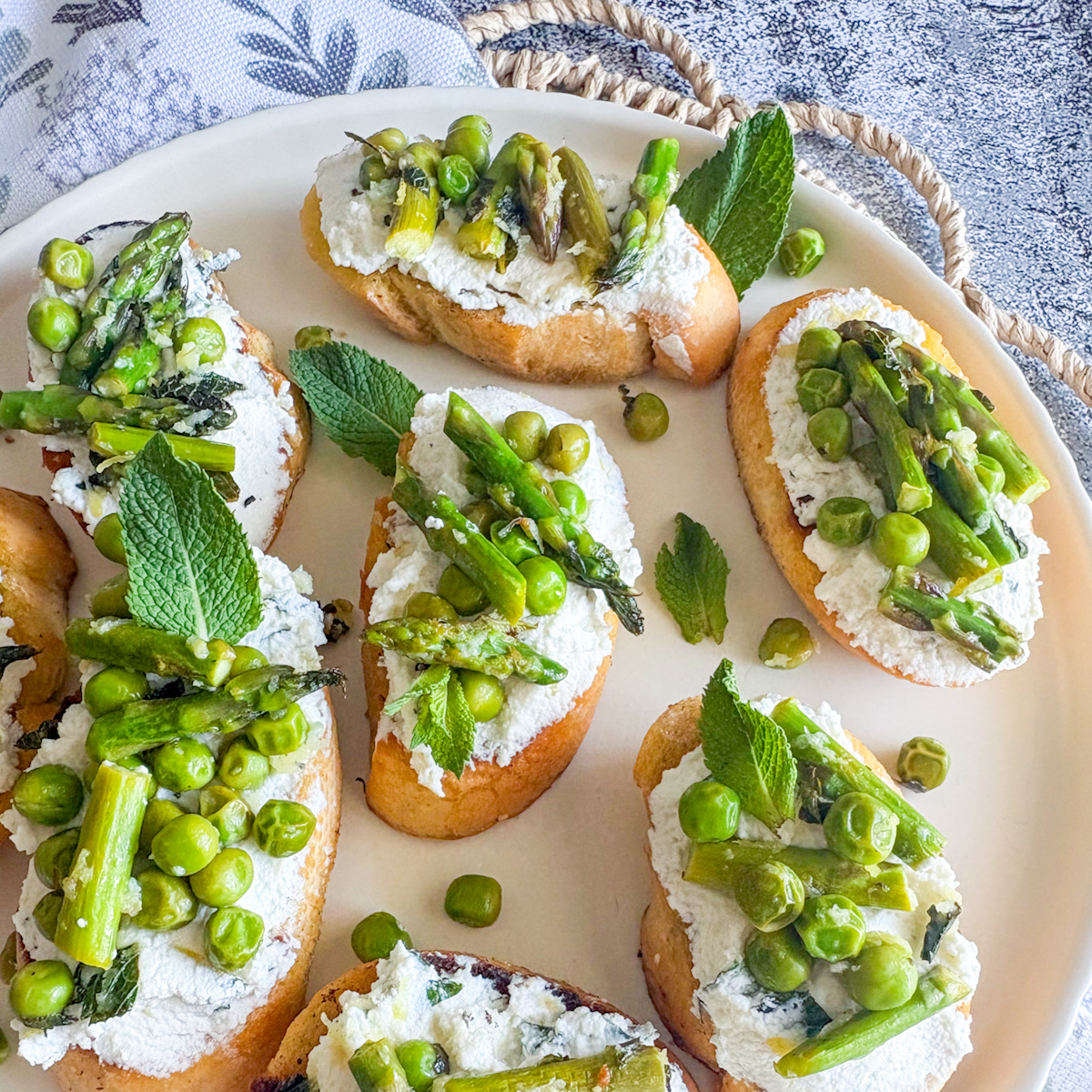 Plate of pea and asparagus crostini topped with ricotta, mint leaves and spring veg