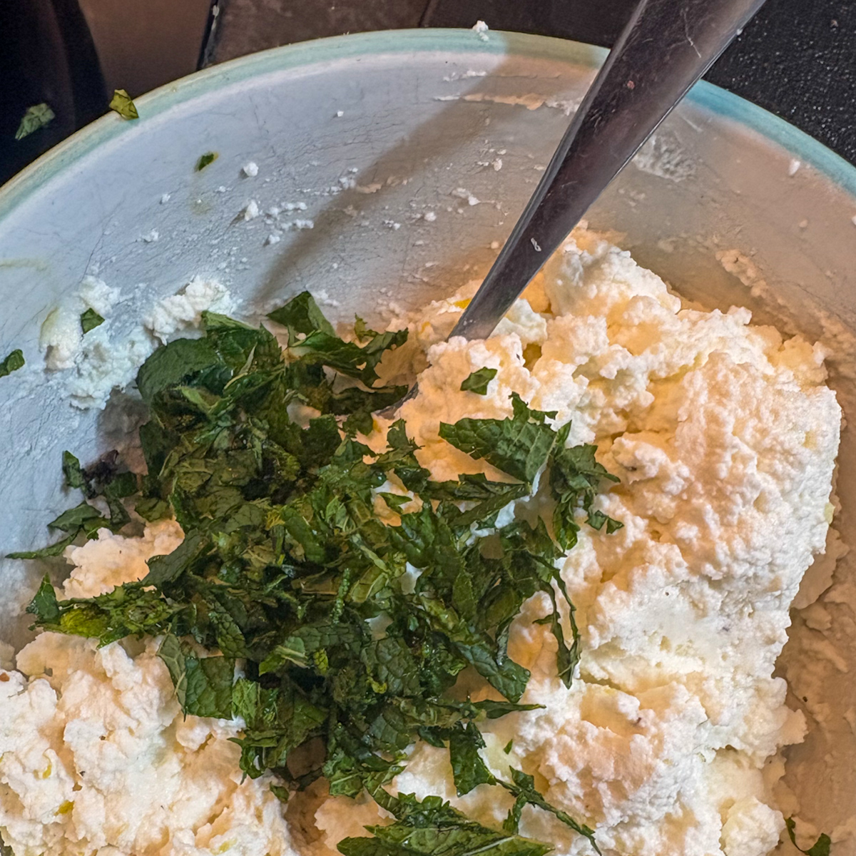 Whipped ricotta mixture with chopped fresh mint in a bowl for pea and asparagus crostini