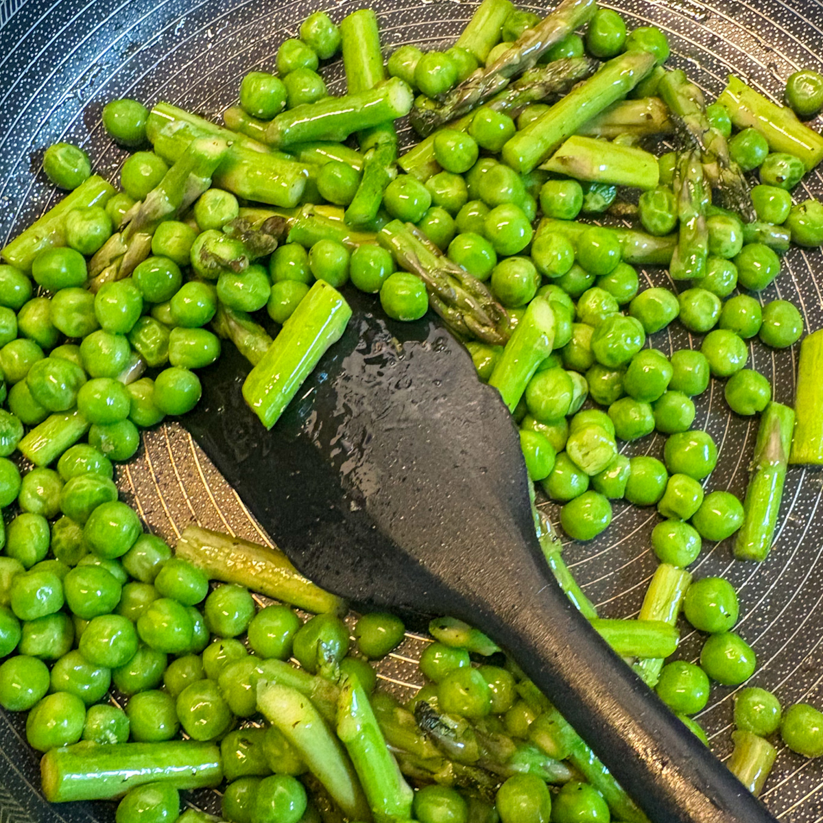 Fresh peas and chopped asparagus sautéing in a pan for pea and asparagus crostini topping