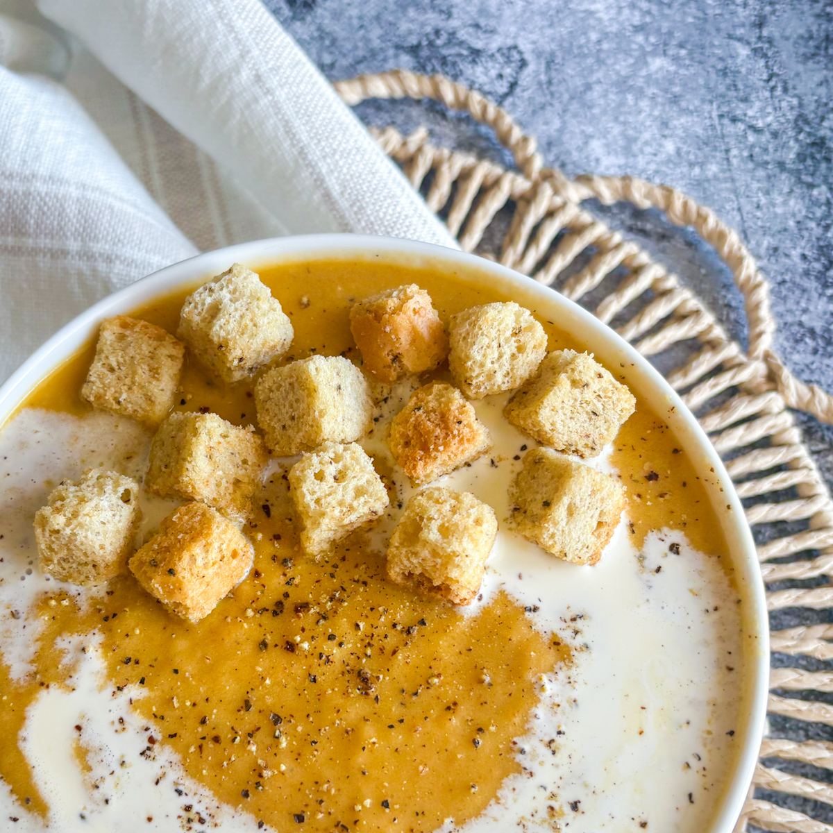 Close up of creamy roasted root vegetable soup with golden croutons, cream swirl and black pepper