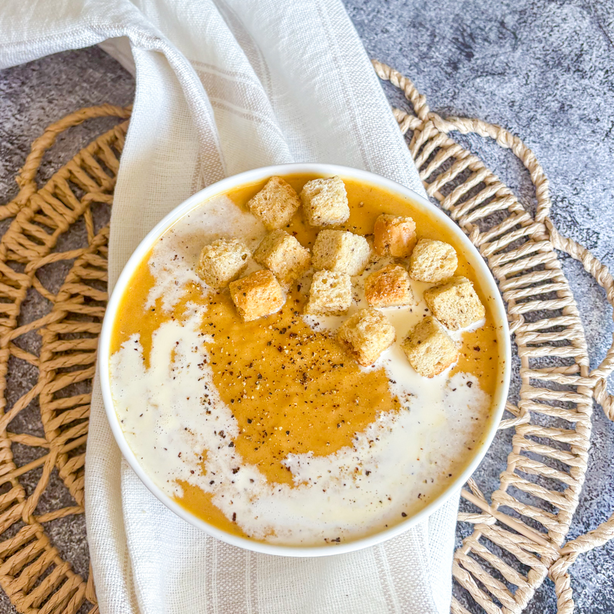 Top down view of creamy roasted root vegetable soup with golden croutons and a swirl of double cream