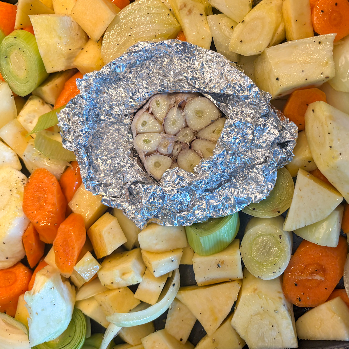 Roasted root vegetable soup prep with chopped carrots, parsnips, turnip, leek and foil-wrapped garlic head