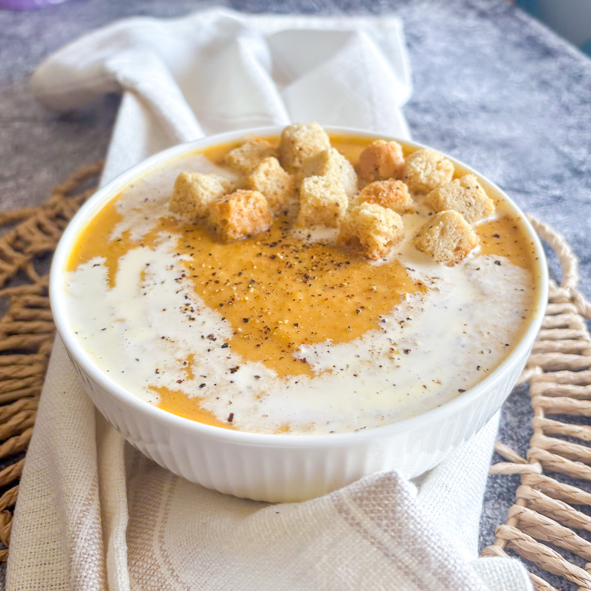 Homemade roasted root vegetable soup bowl topped with crunchy croutons, cream swirl and black pepper
