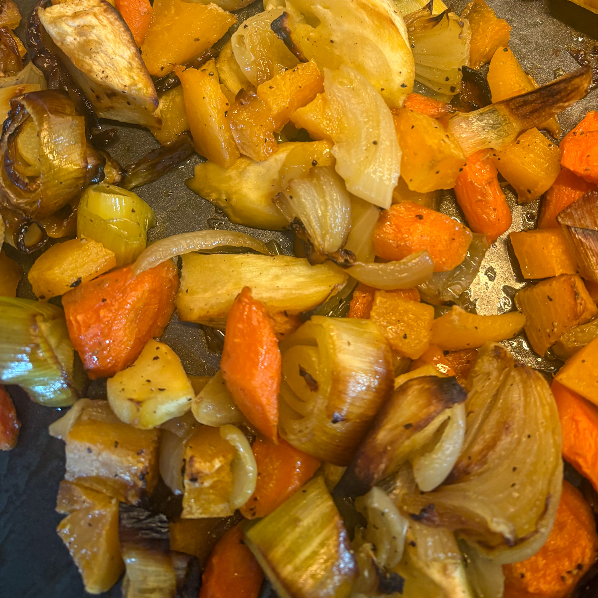 Caramelised root vegetables on baking tray for roasted root vegetable soup with golden carrots, parsnips and leeks