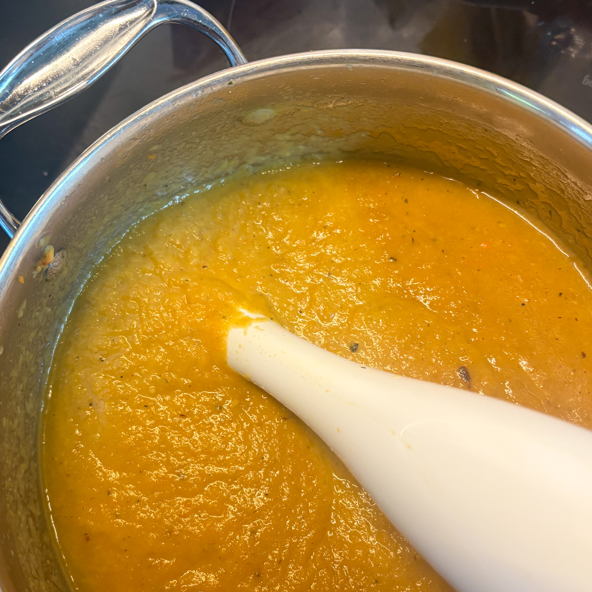 Pot of blended roasted root vegetable soup with immersion blender, showing smooth golden texture