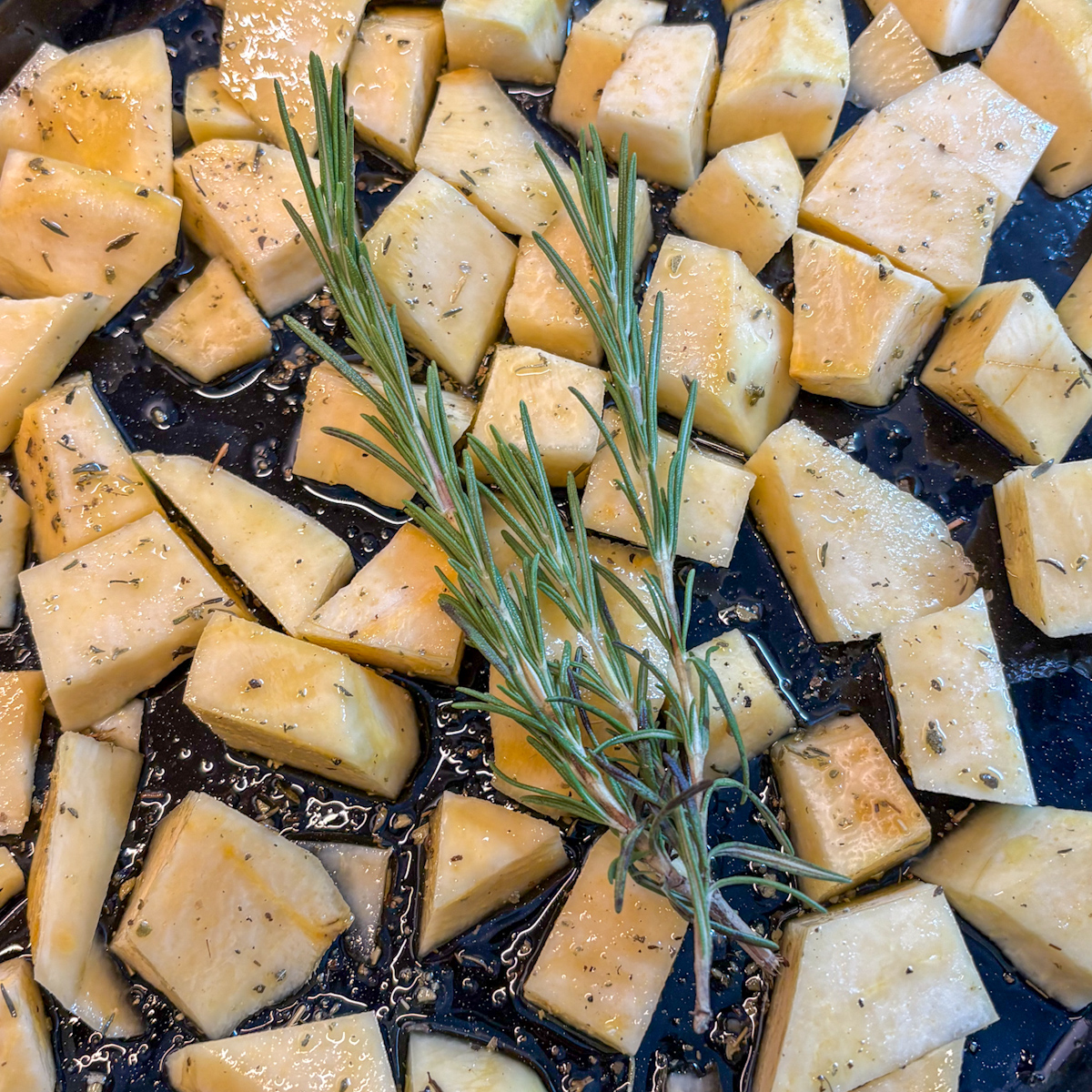 Raw turnip pieces tossed in olive oil and herbs with rosemary sprigs on tray