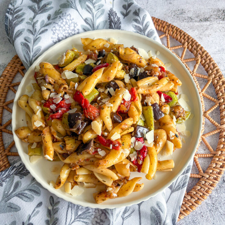 Hearty plate of roasted vegetable pasta with courgette, aubergine and peppers topped with parmesan