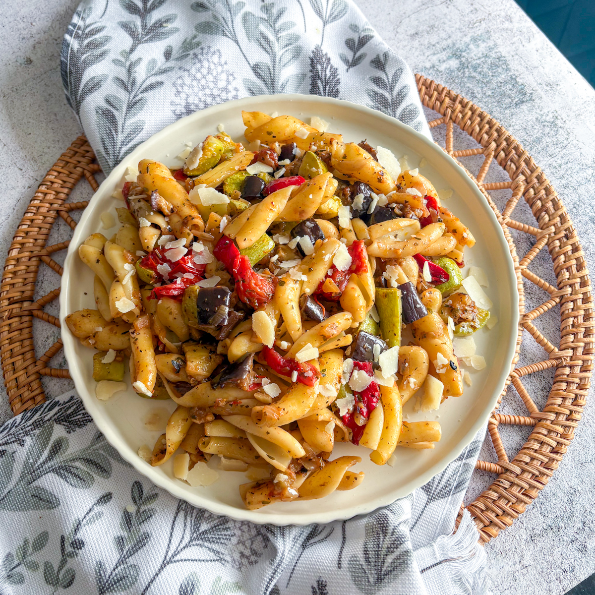 Top-down shot of roasted vegetable pasta with golden vegetables and shaved parmesan flakes