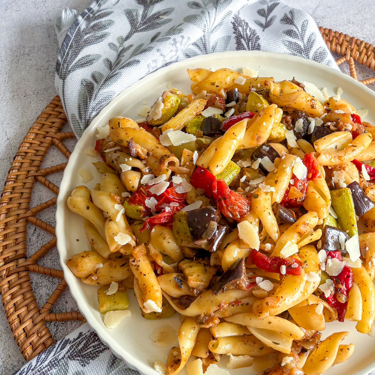 Roasted vegetable pasta served on a white plate with a botanical napkin and rustic styling