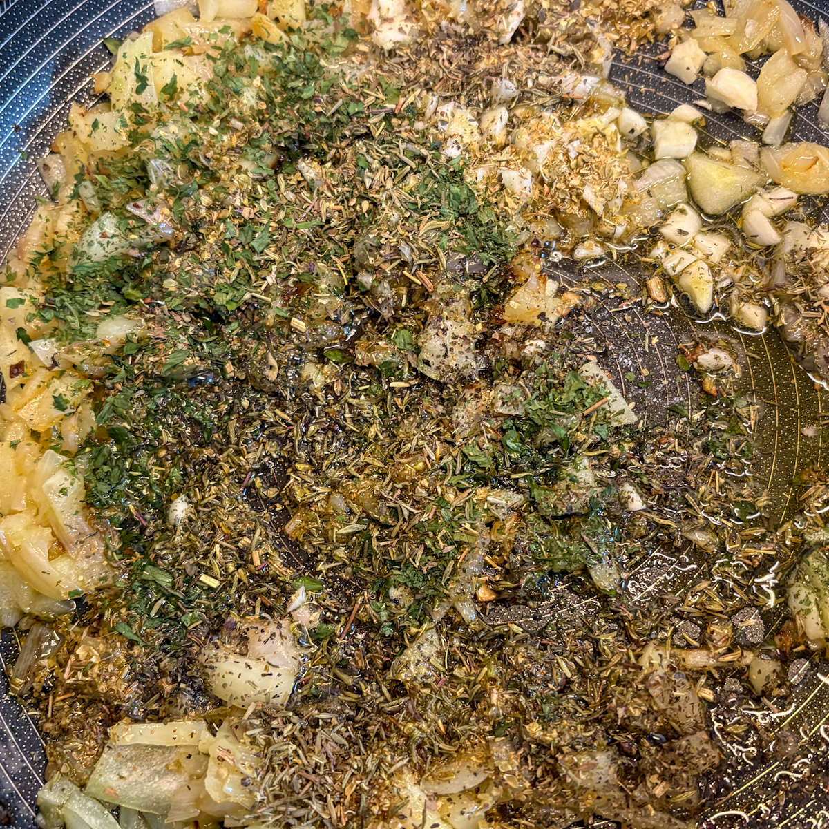 Onion, garlic and Italian herbs sautéing in a skillet for roasted vegetable pasta sauce base