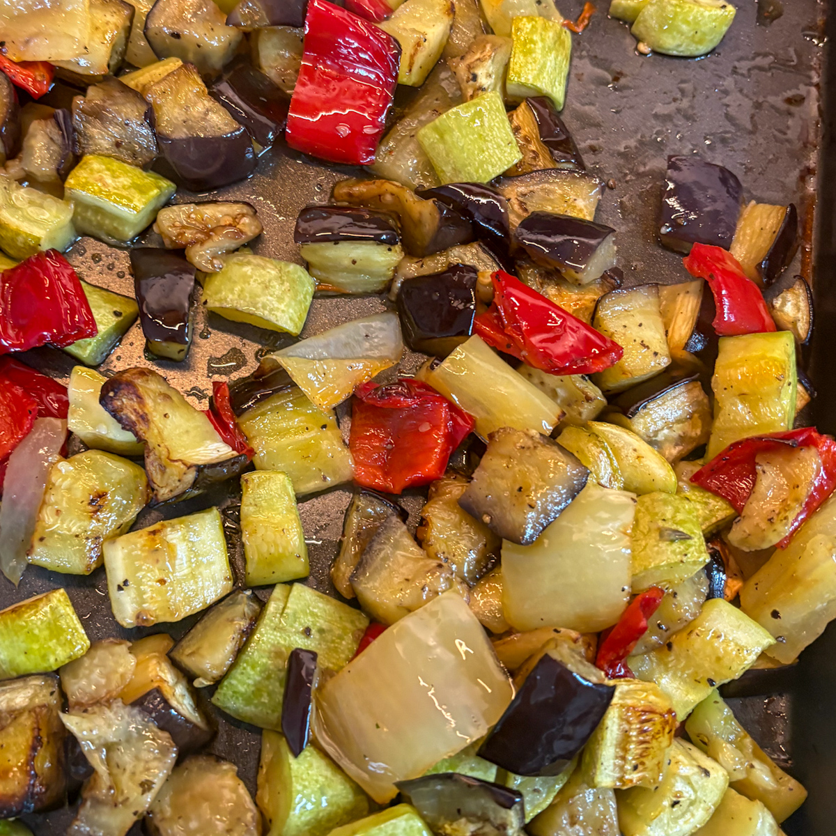 Aubergine, courgette and red peppers on a baking tray for homemade roasted vegetable pasta