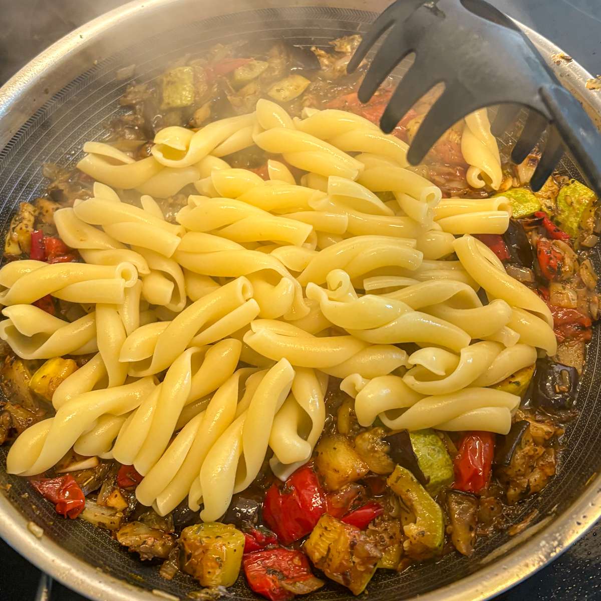 Cooked pasta added to skillet with roasted vegetables for easy roasted vegetable pasta recipe