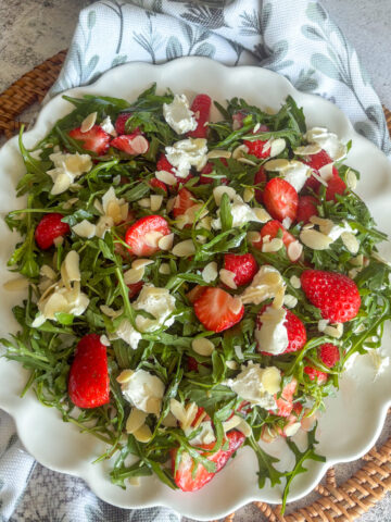 Strawberry rocket salad served on a white plate with mascarpone and flaked almonds