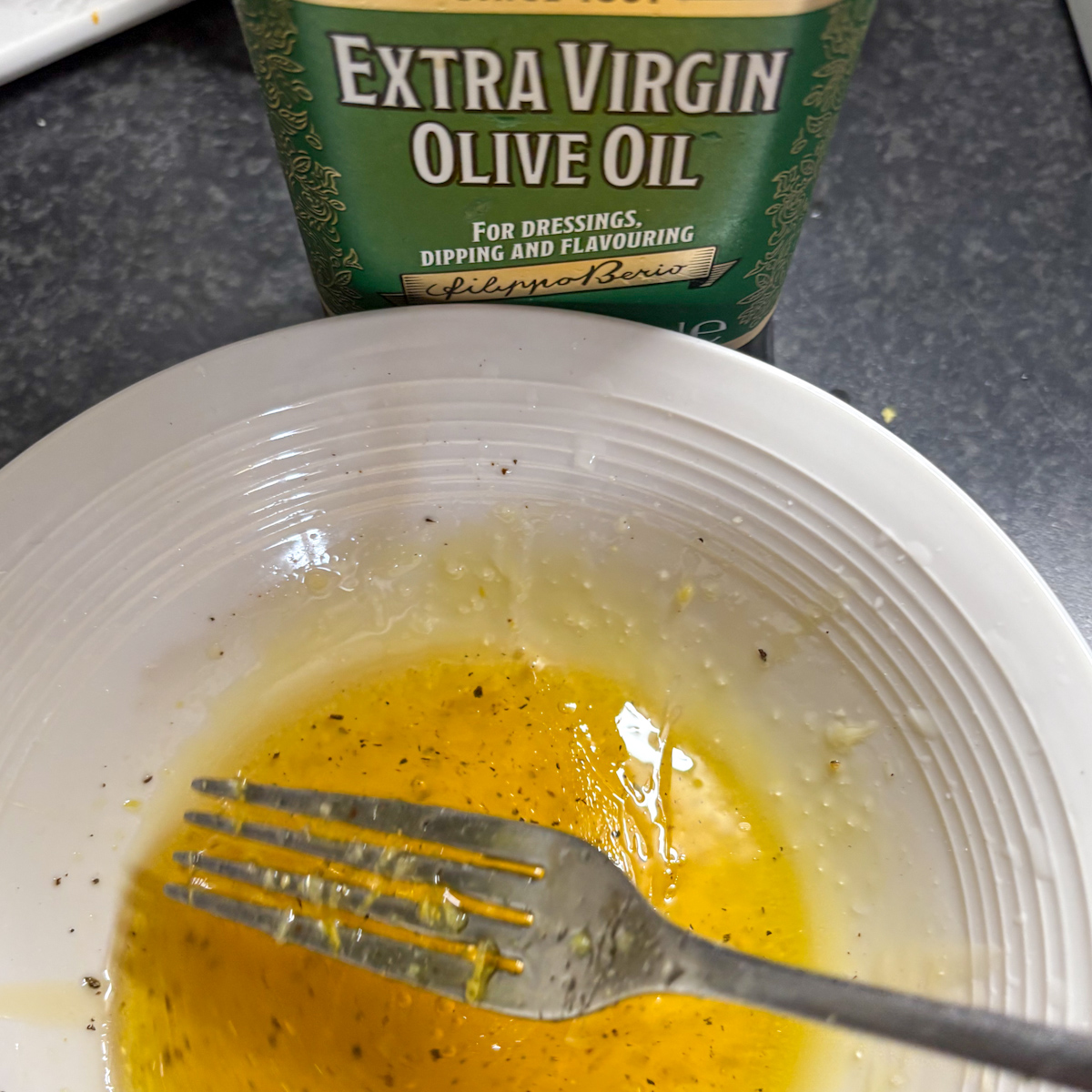 Honey lemon and olive oil dressing for strawberry rocket salad whisked in a bowl beside olive oil