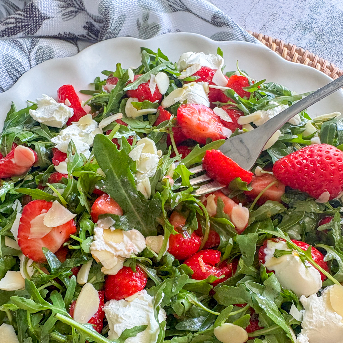 Fork lifting a bite of strawberry rocket salad with mascarpone and flaked almonds