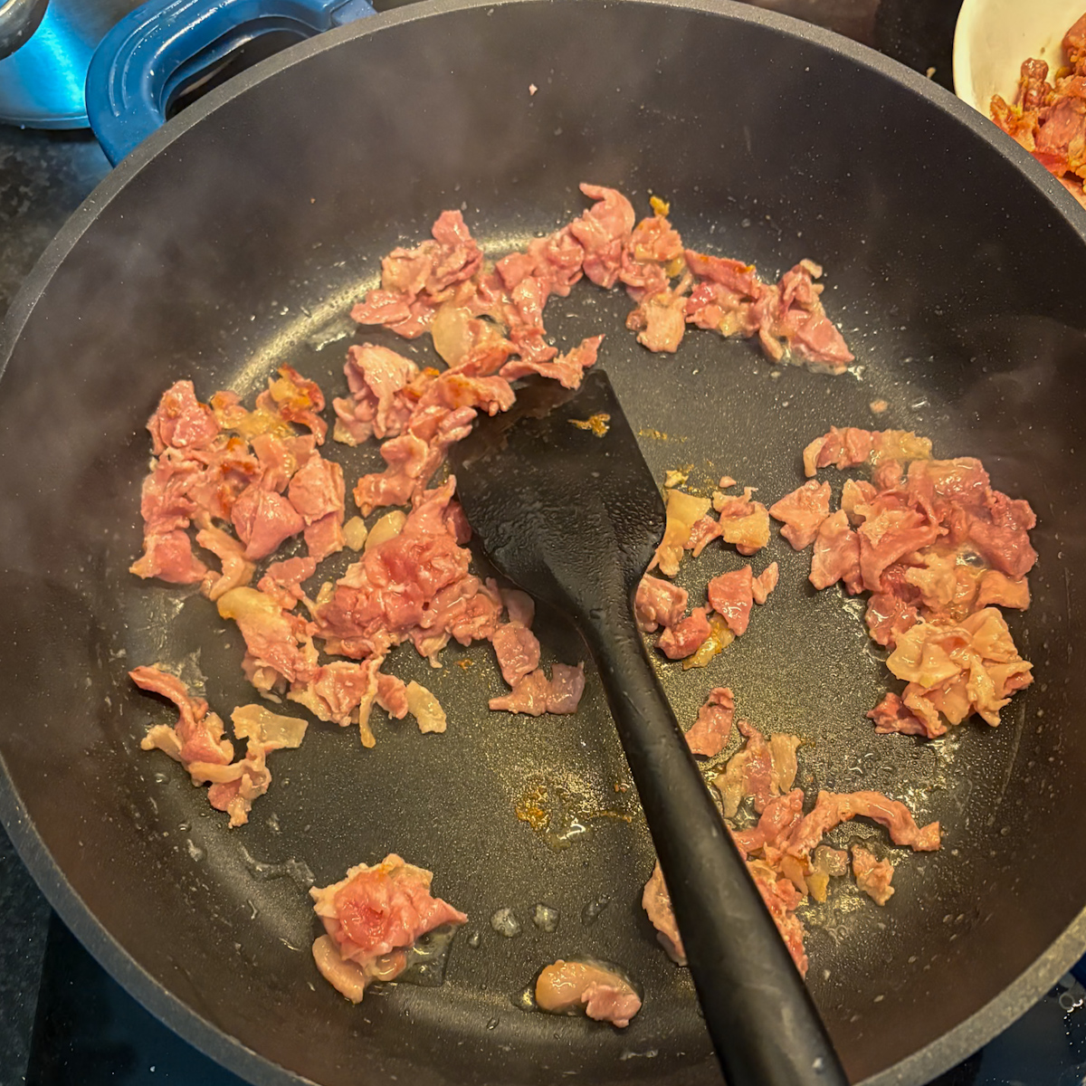 Frying bacon offcuts until crispy for breakfast dirty rice in a pan