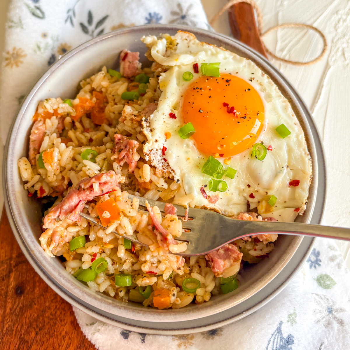 Breakfast dirty rice with bacon and eggs served with a fork in a grey bowl