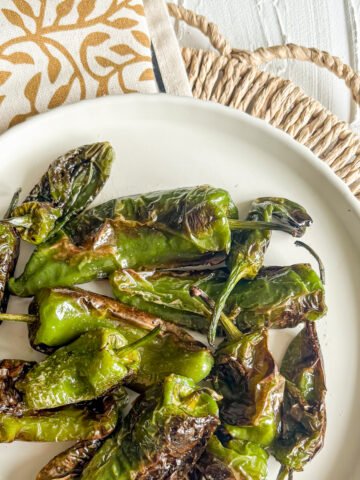 Blistered padron peppers on a white plate with olive oil and sea salt