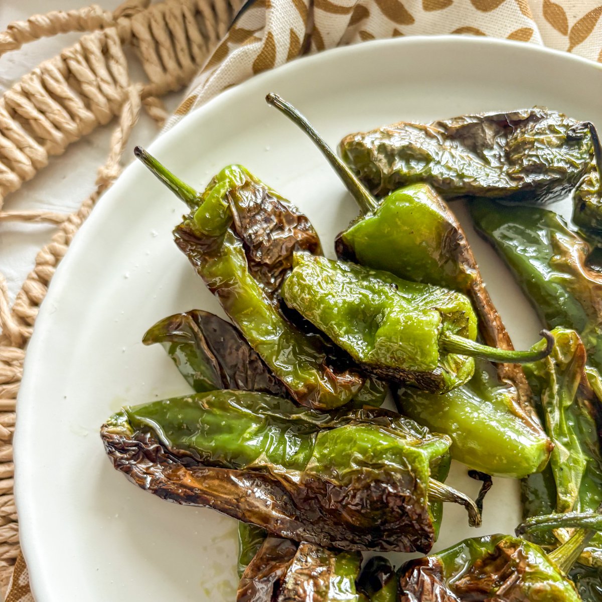 Blistered padron peppers with charred skins on a white plate
