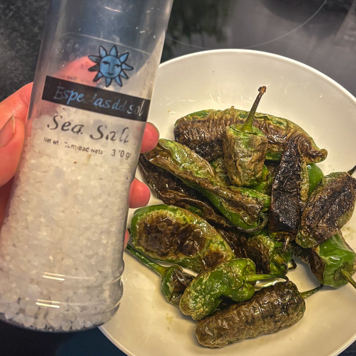 Fried padron peppers being seasoned with sea salt from a grinder