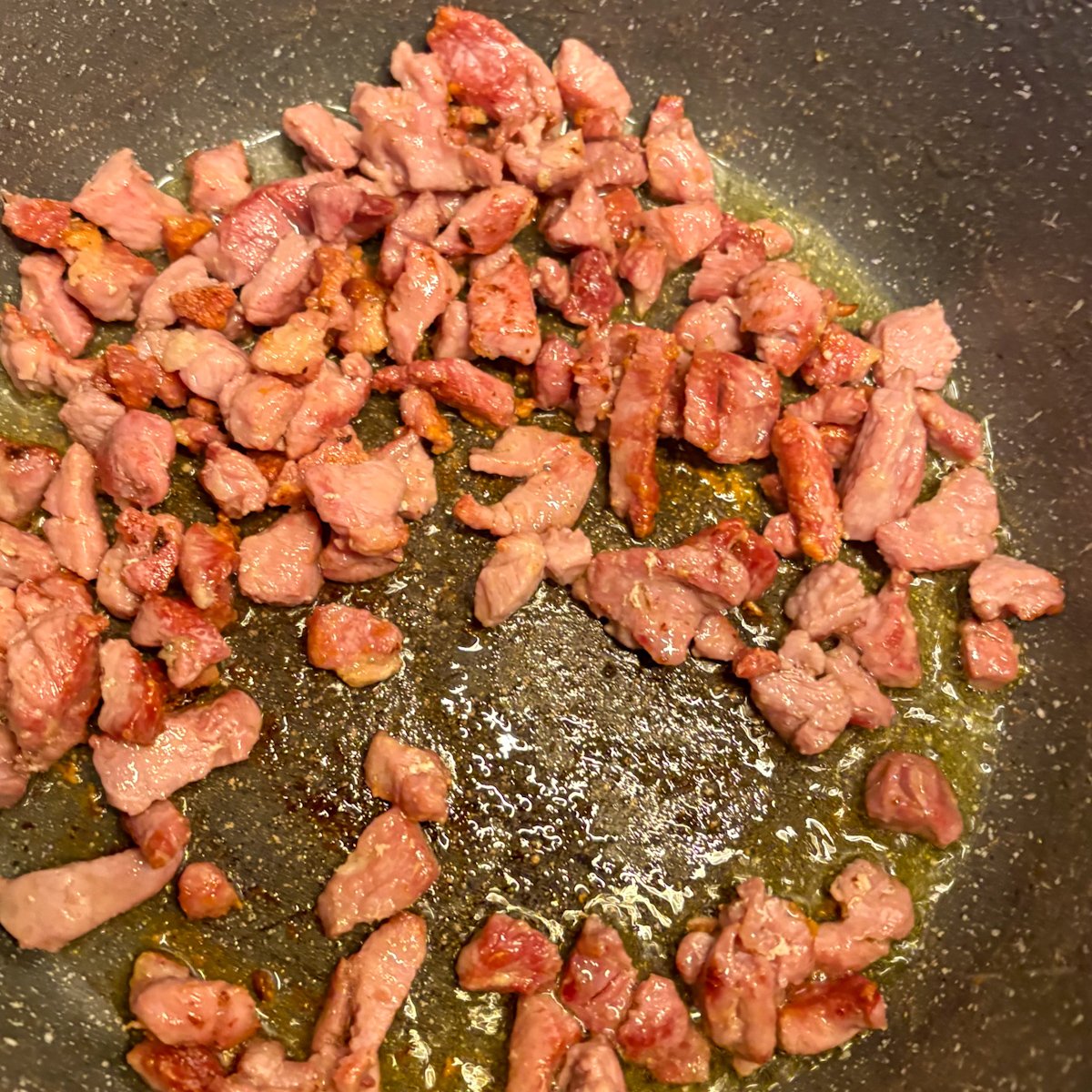 Bacon offcuts frying golden in olive oil — first step of peas with bacon and ricotta