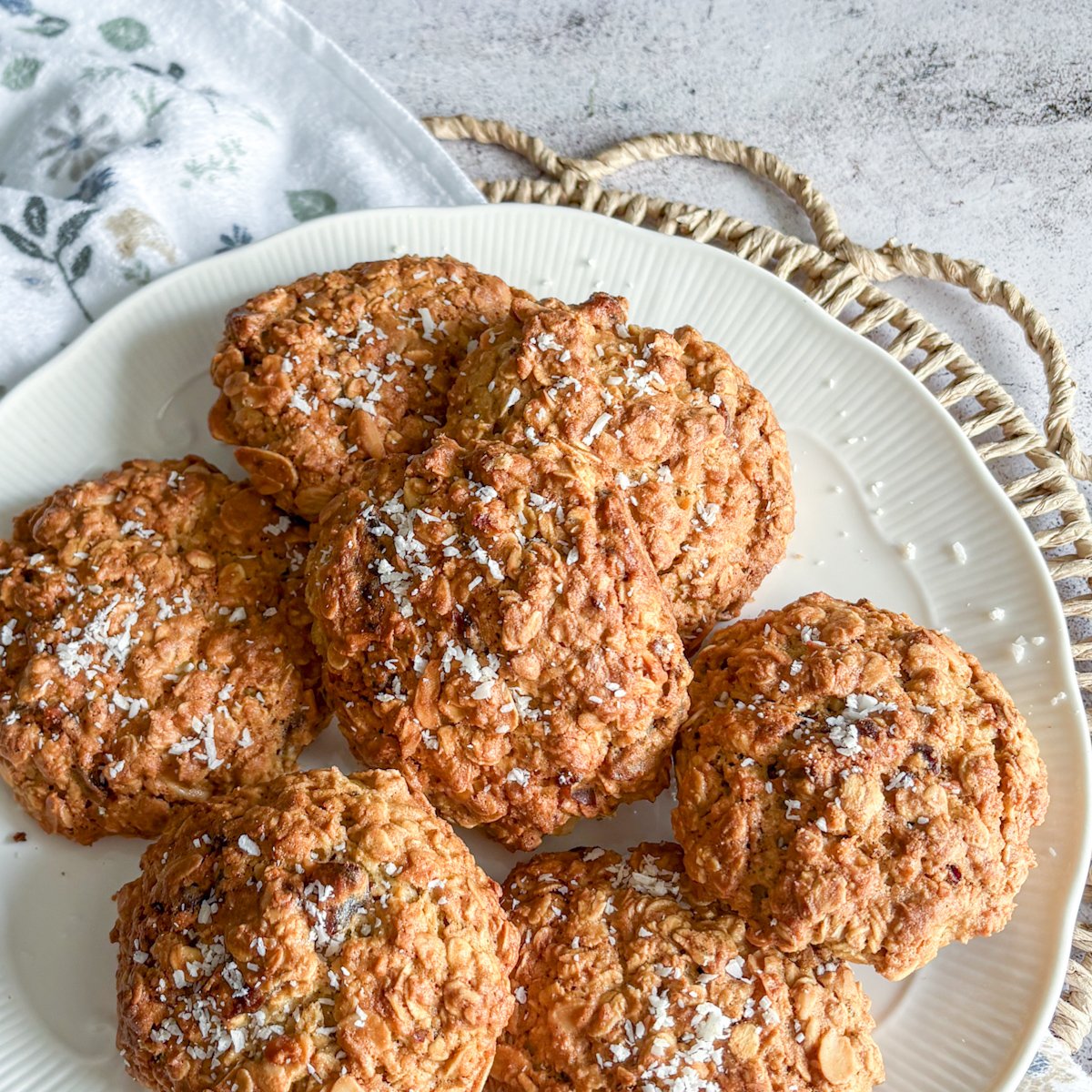 Oatmeal cookies with dates and almonds arranged on a white plate, dusted with coconut