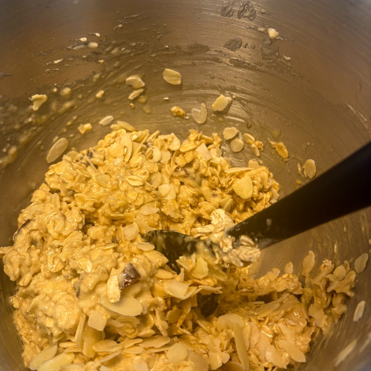 Oatmeal cookie dough with dates, oats and flaked almonds folded together in a mixing bowl