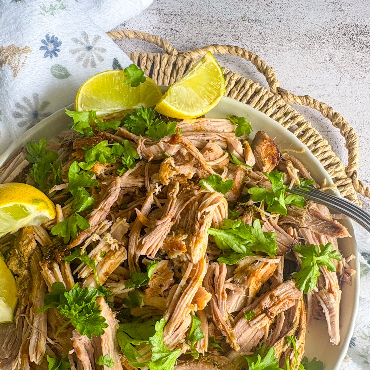  Cuban mojo pork plated with lemon and lime wedges, fresh parsley and a fork on a floral napkin