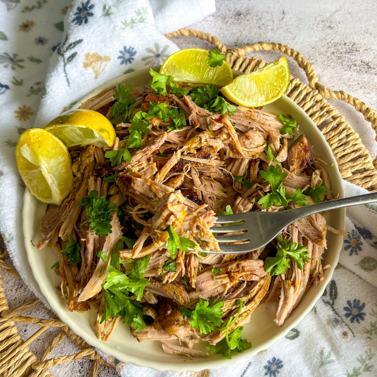  Tender shredded mojo pork lifted on a fork above a plate with lime wedges and parsley
