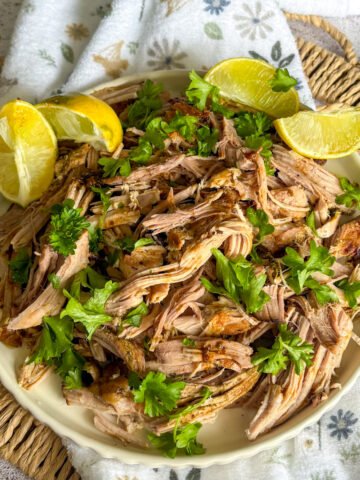Slow cooker mojo pork plated overhead with lemon, lime wedges and fresh herbs on a woven mat