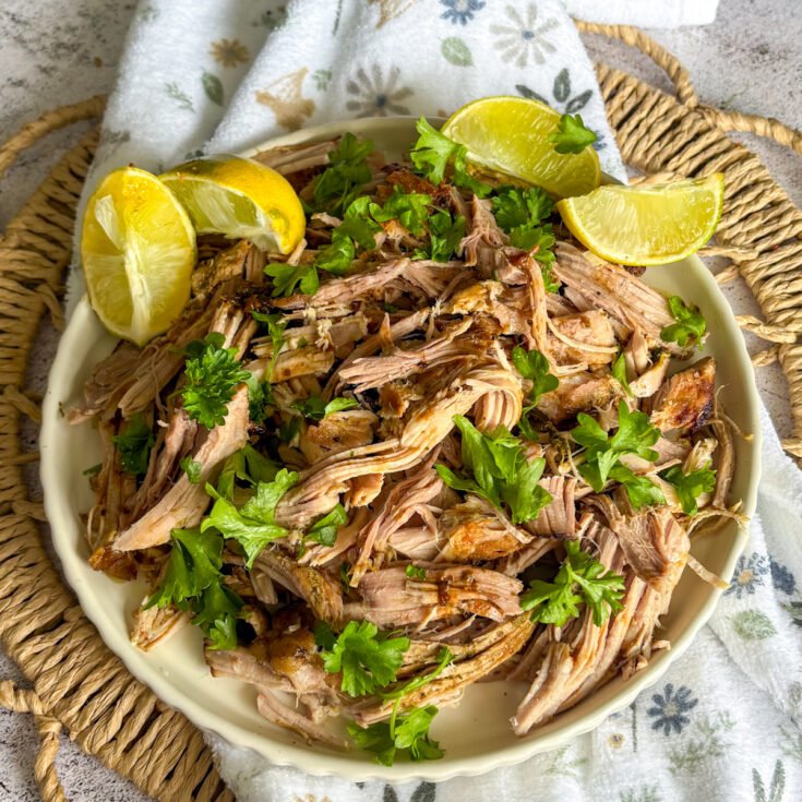 Slow cooker mojo pork plated overhead with lemon, lime wedges and fresh herbs on a woven mat