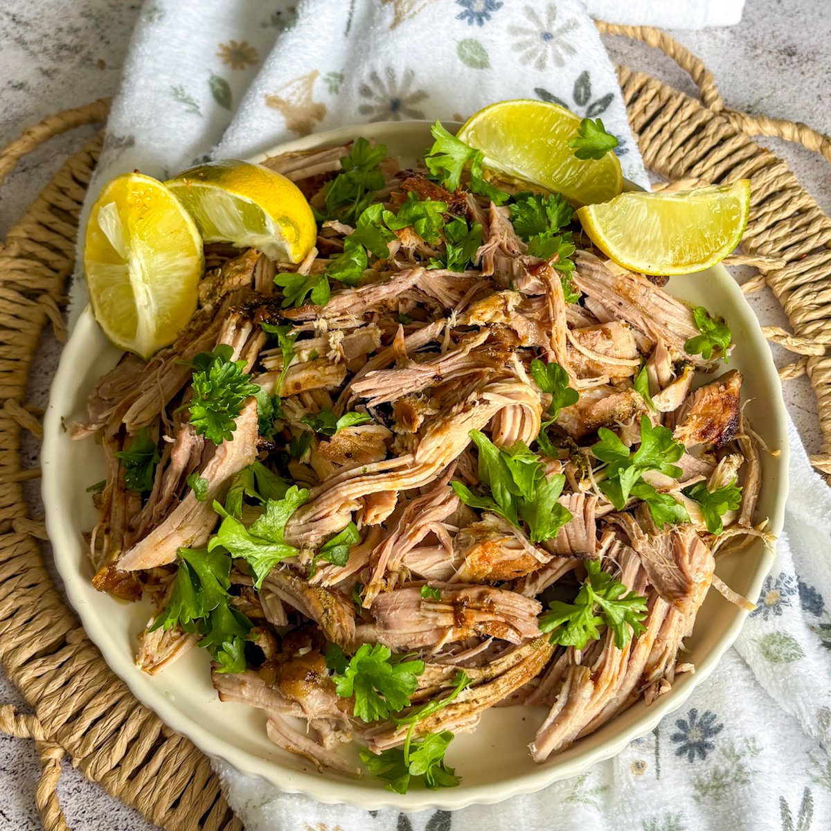  Slow cooker mojo pork plated overhead with lemon, lime wedges and fresh herbs on a woven mat