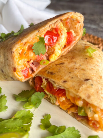 Breakfast burritos cut in half on a plate, showing bacon, egg and tomato filling
