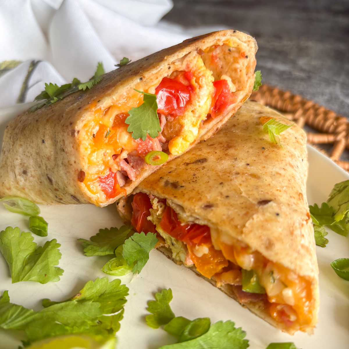 Breakfast burritos cut in half on a plate, showing bacon, egg and tomato filling