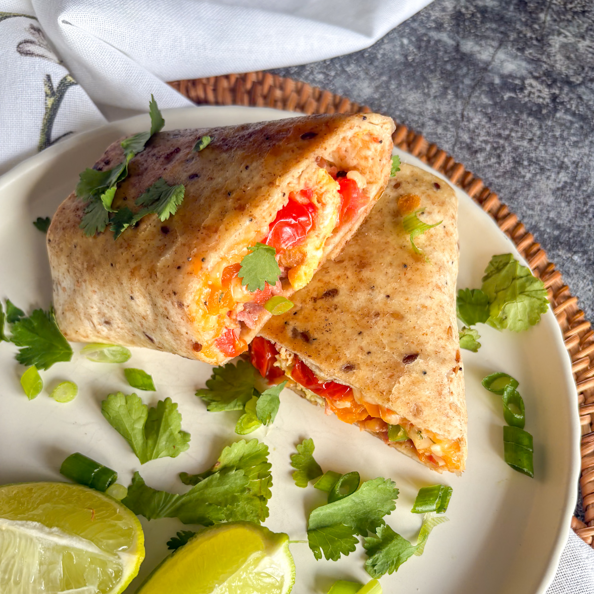 Savoury breakfast burritos with cheddar and tomato, served with lime wedges
