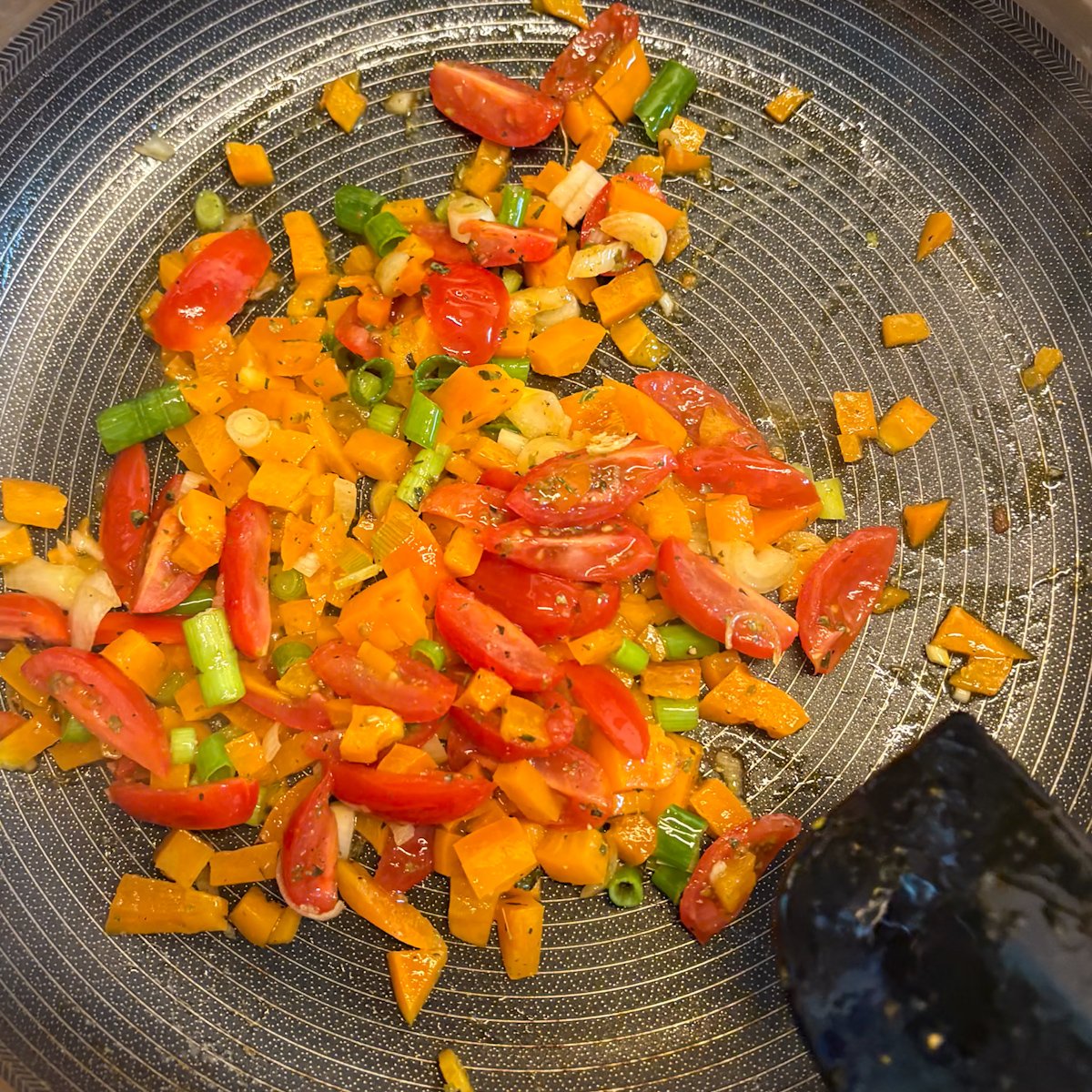Diced peppers, tomatoes and spring onion sautéing in a pan for breakfast burritos
