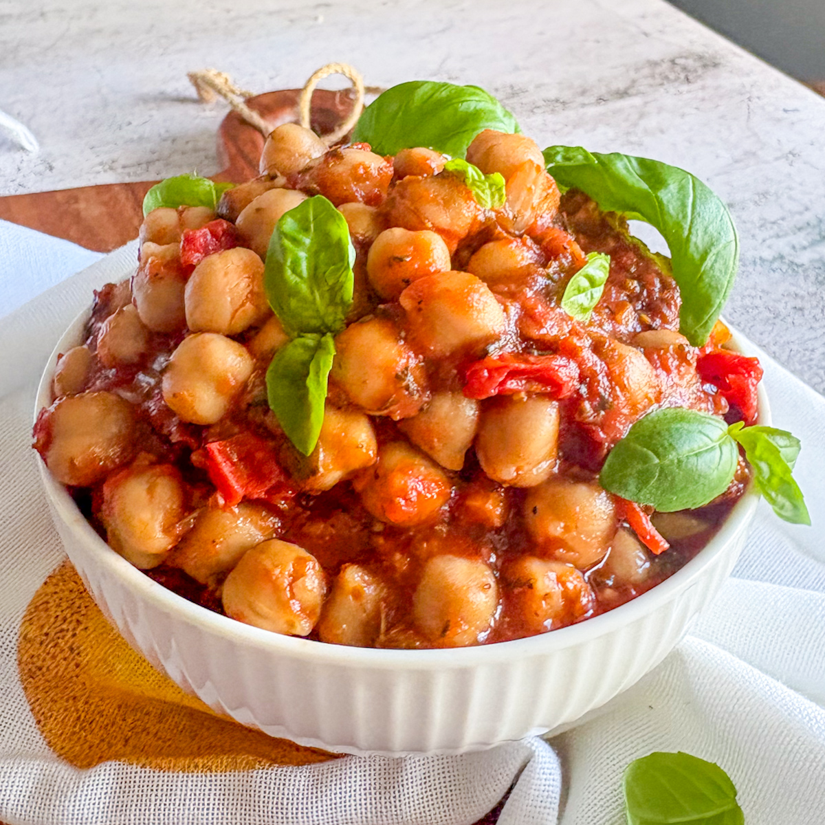 Chickpeas in tomato sauce in a white bowl, topped with fresh basil leaves