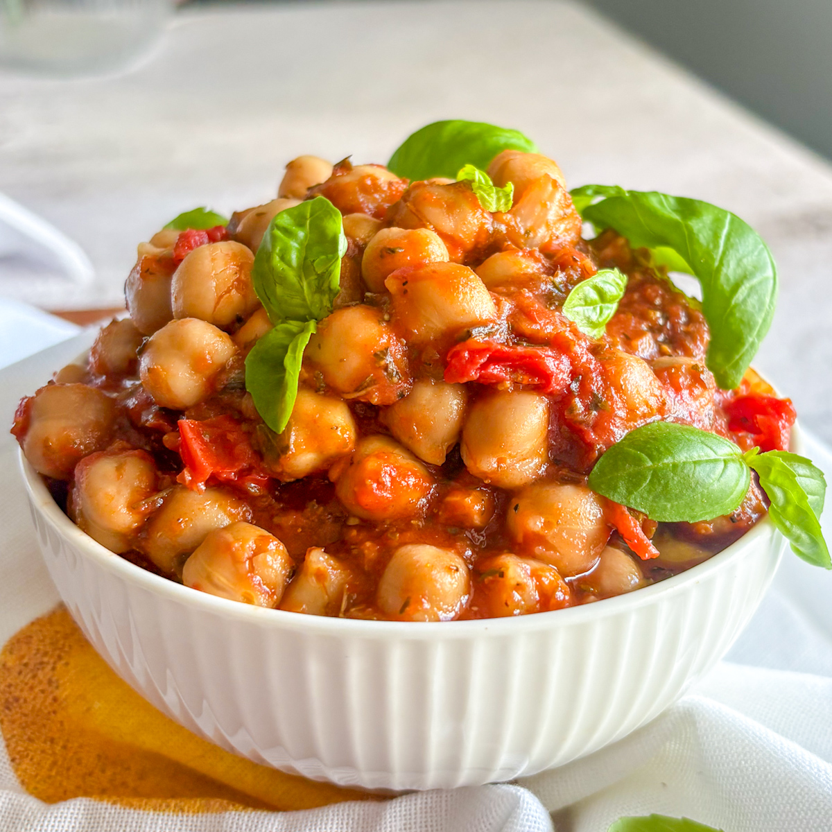 Hearty chickpeas in tomato sauce served in a white bowl with basil on top
