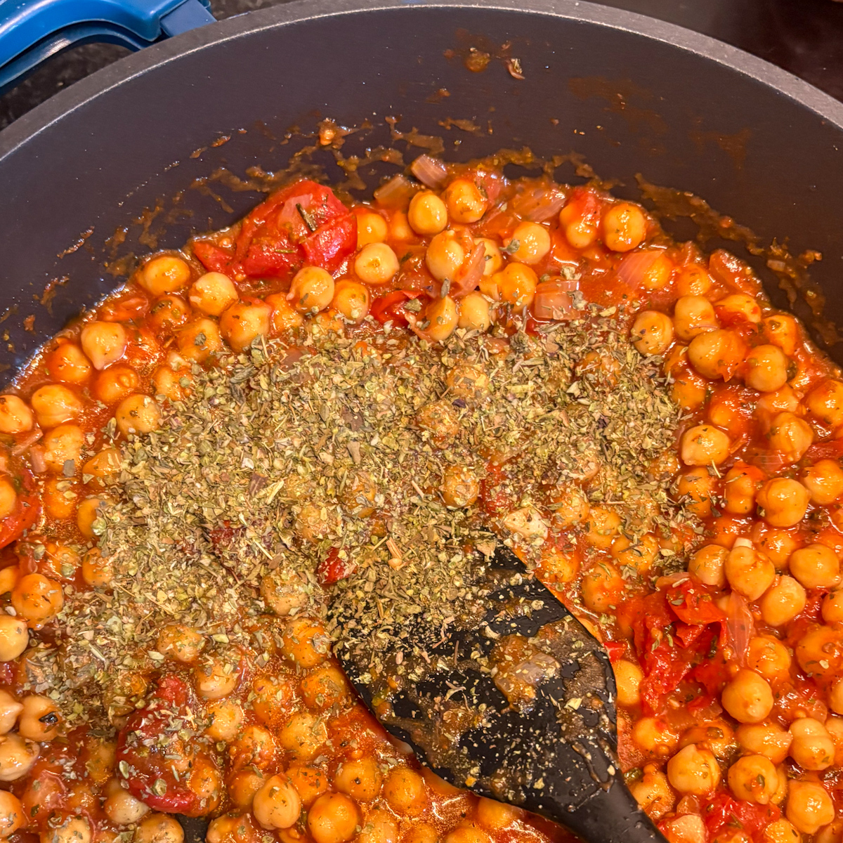 Chickpeas in tomato sauce with dried herbs added in the pan